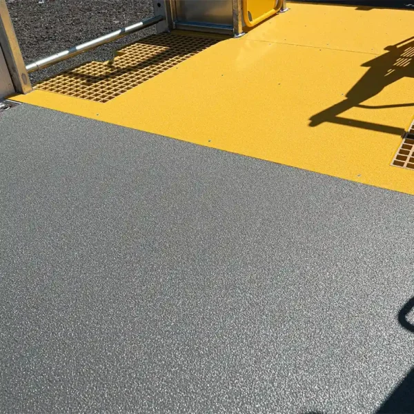 An Anti-Slip Flat Sheet in textured grey is installed beside a bright yellow section, separated by a metal barrier. The shadow of playground equipment falls across the yellow area.