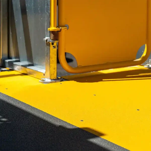 A close-up of the Anti-Slip Flat Sheet in bright yellow, featuring a yellow rail and metal support—possibly at a bus entrance—sunlit and casting shadows.