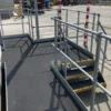 The Anti-Slip Flat Sheet is installed on a metal platform with safety railings and stairs outdoors, set on concrete with striped warning posts nearby and industrial vehicles visible in the background.