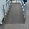 An Anti-Slip Flat Sheet covers the wheelchair ramp with metal railings on both sides, providing a textured, slip-resistant surface leading up to the building entrance and bordered by a paved area.