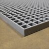 A close-up of the Open Top Grating shows its metallic grey finish and grid pattern with square openings, placed on a concrete floor.