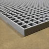 A close-up of the Open Top Grating shows its sturdy, industrial metal grid with square openings, placed on a smooth brown surface.