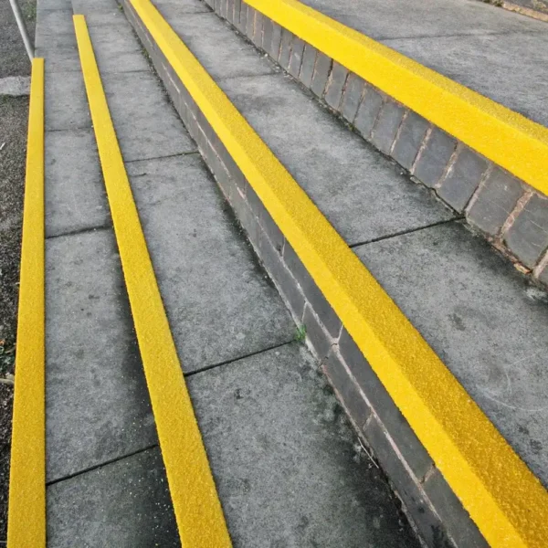 Anti-Slip Stair Nosing with yellow strips installed on concrete steps to enhance pedestrian visibility and safety, featuring a brick side wall, photographed at an angle.
