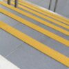 Anti-Slip Stair Nosing in grey with bright yellow safety strips improves step visibility and prevents slipping. Stainless steel railings are installed at the top.