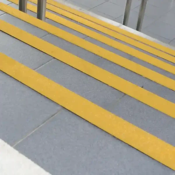 Outdoor stairs feature grey tiles and Anti-Slip Stair Nosing in bright yellow on each step for safety. Stainless steel handrails are visible at the top of the steps.