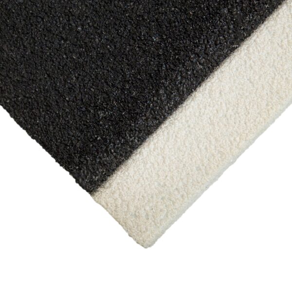 Close-up of an Anti-Slip Stair Tread showing a rough, textured black surface meeting a lighter, off-white strip at the corner, creating a sharp visual contrast.