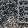 Close-up of a 16mm Black Grass Mat with textured circular and knobbed patterns, scattered gravel, and a pair of yellow ants near the centre.