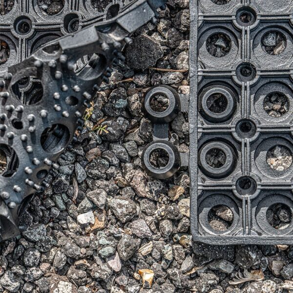 Close-up of a 16mm Black Grass Mat with textured circular and knobbed patterns, scattered gravel, and a pair of yellow ants near the centre.