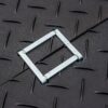 The 2-Way Connector, a square-shaped metal frame, rests on a dark textured surface featuring a diagonal seam and raised diamond-shaped patterns.
