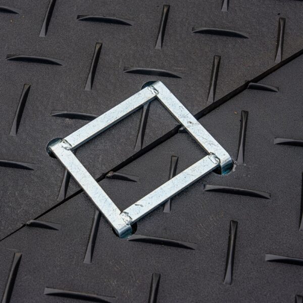 The 2-Way Connector, a square-shaped metal frame, rests on a dark textured surface featuring a diagonal seam and raised diamond-shaped patterns.