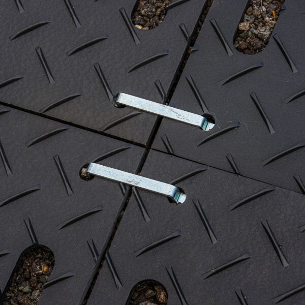 Two 2-Way Connectors secure black, textured interlocking panels with a chequer plate pattern, positioned on a gravel surface.