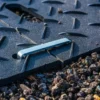 A 2-Way Connector rests on a textured black rubber mat with grooves, surrounded by small gravel stones outdoors.