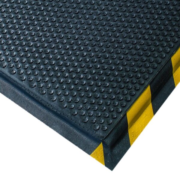 A close-up of the Foam Cushioned Industrial Mat, featuring black rubber with raised circular bumps and yellow-and-black caution stripes on the edges, commonly used in workplaces for safety and anti-fatigue support.