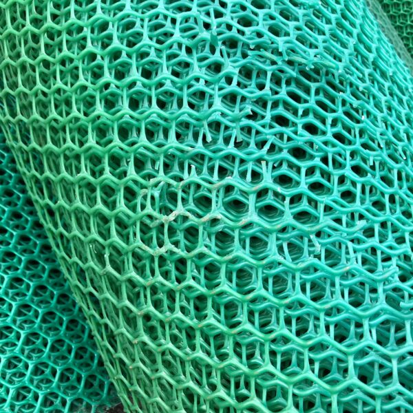 Close-up of stacked Grass Mat Underlay Mesh in turquoise, featuring a hexagonal pattern. The slightly bent and layered mesh highlights its texture, depth, and geometric repetition.