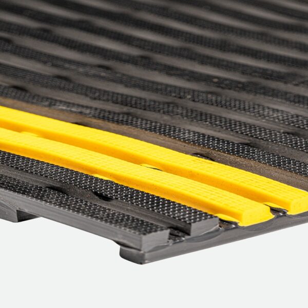 Close-up of the Self-Draining Safety Mat features a textured black rubber surface with raised, angled grooves and two bright yellow strips running parallel across it.