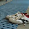 A pair of white trainers with black and grey accents and red interiors are displayed on a Cross-Ribbed PVC Leisure Mat placed atop a tiled floor.