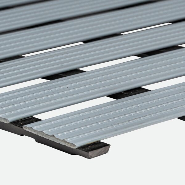 Close-up view of the Cross-Ribbed PVC Leisure Mat in light grey, featuring parallel ribbed slats with dark gaps between them, resembling industrial flooring or a grating.