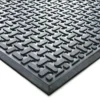 Close-up of the Nitrile Workplace Mat, a black rubber floor mat with a raised, repeating geometric pattern of interlocking curves, shown at an angle to highlight its texture and thickness.
