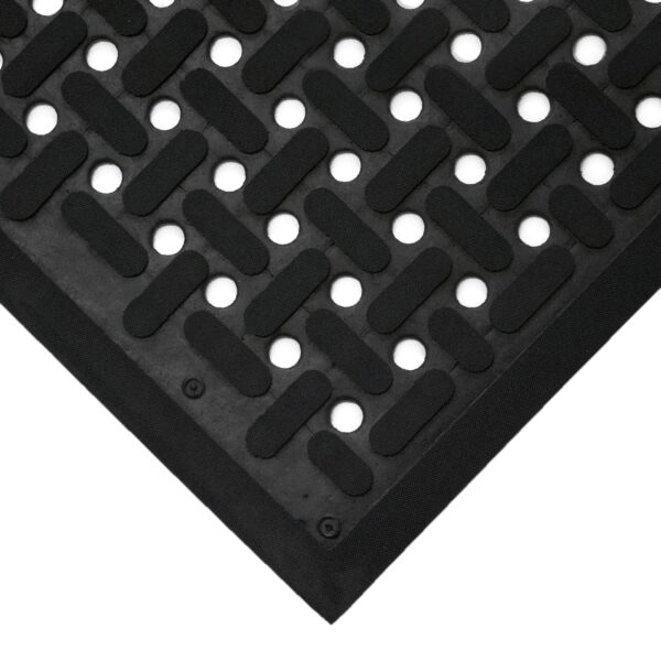 Close-up of a Nitrile Workplace Mat corner showing its black rubber surface with a textured pattern of raised horizontal bars and round holes for slip-resistance and drainage.