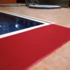 A red leisure mat is placed along the edge of an indoor pool with tan tiled flooring, and another pool or hot tub can be seen in the background.
