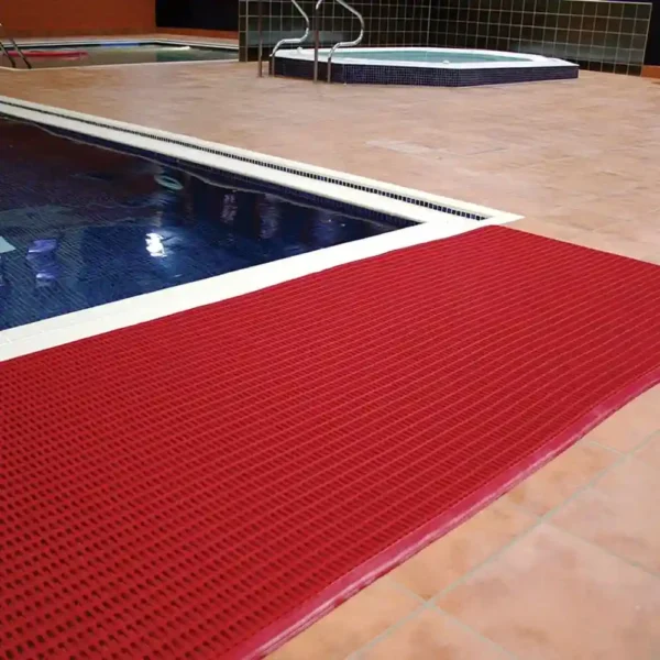 A red leisure mat is placed along the edge of an indoor pool with tan tiled flooring, and another pool or hot tub can be seen in the background.