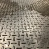 Close-up of the Chequer Plate Interlocking Tile, featuring a metal diamond plate pattern with raised oval-shaped ridges in a repeating design. Certain sections appear shinier, likely from light reflection or cleaning.