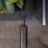 A black cable runs along a grey carpet, covered by a PVC Cable Protector, next to the leg of a table and a potted plant with green leaves.