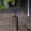 A black cable runs under a PVC Cable Protector on a grey carpeted floor, next to a black table with green leaves partially visible on top.