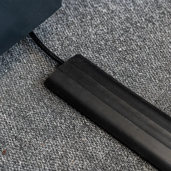 The PVC Cable Protector shields a lead on a grey carpeted floor, organising it and preventing tripping.