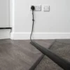 A black cable runs from a wall socket, shielded by the PVC Cable Protector as it crosses from hard floor to carpet in a room corner.
