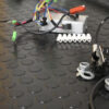 Close-up of electrical and mechanical components, such as wires, connectors, and metal parts, arranged on Circular Stud Rubber Matting with a black, textured circular pattern.