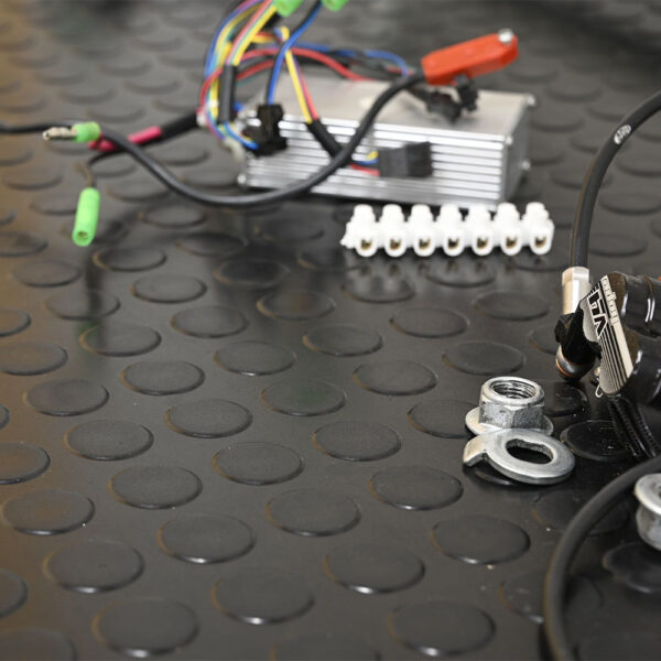 Close-up of electrical and mechanical components, such as wires, connectors, and metal parts, arranged on Circular Stud Rubber Matting with a black, textured circular pattern.