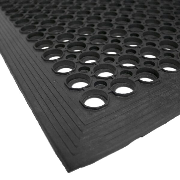 Close-up of the Drainage Top Mat, a black rubber mat featuring large and small circular holes and a textured border along the edges.