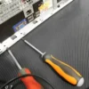 Two screwdrivers and a cable rest beside a computer's back panel showing USB, VGA, and audio jacks, all situated on Electrical Insulation Matting with a black ribbed surface.