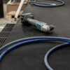A cordless power drill and a blue air hose rest on Fine Ribbed Rubber Matting in a workshop, with cardboard boxes and other tools visible in the background.