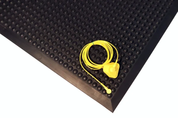 A yellow wired device with a clip is coiled and placed on a Bubble Top ESD Mat, featuring a textured black rubber surface with raised circular bumps.