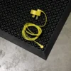 A yellow earphone with a matching plug is coiled and placed on a Bubble Top ESD Mat, which has a textured black surface, next to a grey concrete floor.