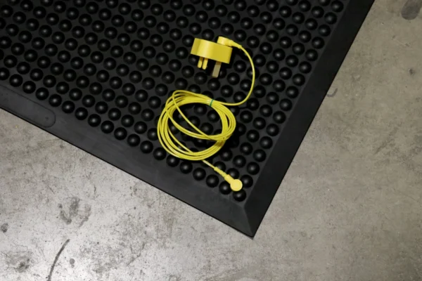 A yellow earphone with a matching plug is coiled and placed on a Bubble Top ESD Mat, which has a textured black surface, next to a grey concrete floor.