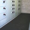 A room with grey electrical switchgear cabinets featuring black and red handles lines the left wall, while Electrical Insulation Matting is placed on the floor beside the cabinets. The walls are constructed of breeze blocks.