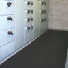 A black Electrical Insulation Matting is placed on the floor in front of electrical control panels with switches in an industrial setting with concrete block walls.