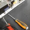 Two screwdrivers rest on Electrical Insulation Matting, positioned near a computer’s back panel displaying VGA, USB, and Ethernet ports.