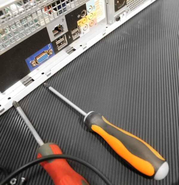 Two screwdrivers rest on Electrical Insulation Matting, positioned near a computer’s back panel displaying VGA, USB, and Ethernet ports.