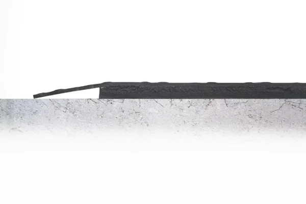 The Senso Dial Mat ESD, a black rubber strip, is fitted to the edge of a flat, grey, textured concrete surface and extends beyond it. The background is white and minimalist.