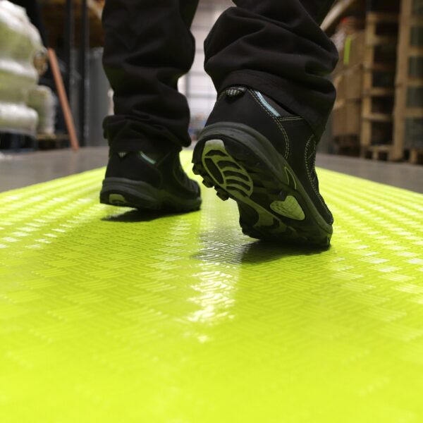 A person in black shoes walks on a bright yellow Construction Site Walkway Roll in an indoor industrial or warehouse setting.