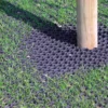 A wooden pole stands on a grassy surface protected by a 16mm Black Grass Mat, which shields the grass and ground around the base of the pole.