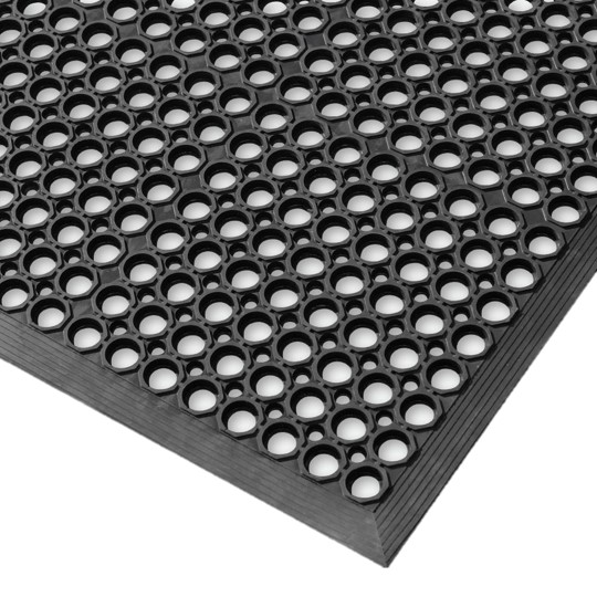 Close-up view of the Honeycomb Kitchen Mat, a black rubber mat featuring regularly spaced circular holes for superior grip and drainage. The angled image highlights the mat’s thickness and textured surface.