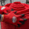 A person wearing red gloves with black fingertips is handling a large roll of Heavy-Duty PVC Vinyl outdoors, possibly during installation or transport.