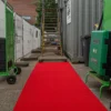 A vivid Heavy-Duty PVC Vinyl Roll stretches between green trolleys and industrial containers, leading to a metal staircase with fencing and a building in the background.