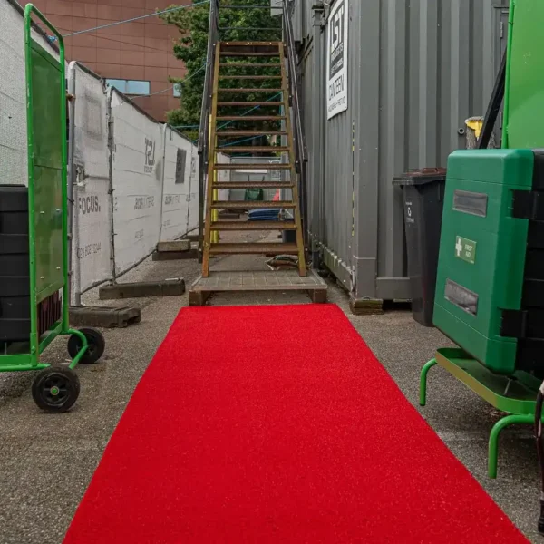 A vivid Heavy-Duty PVC Vinyl Roll stretches between green trolleys and industrial containers, leading to a metal staircase with fencing and a building in the background.