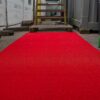 A Heavy-Duty PVC Vinyl Roll in bright red is laid out outdoors, leading up to metal steps surrounded by construction materials and containers.